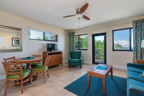 Un salon comprenant une table à manger, des chaises, un téléviseur, un ventilateur de plafond et une vue sur l’extérieur.