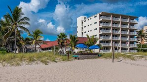 Ett hotell vid stranden med flera balkonger, palmer och ett volleybollnät.