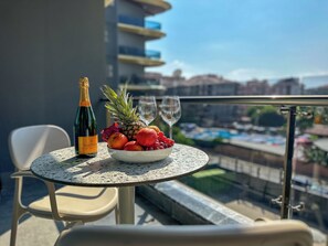 Ein Tisch mit einer Champagnerflasche, einer Obstschale und zwei Weingläsern auf einem Balkon mit Blick auf einen Pool.