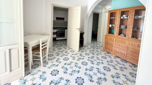 Ein Zimmer mit Esstisch, Stühlen, einer Küche im Hintergrund und einem Schrank mit Glastüren.