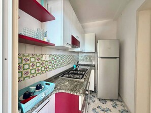 Eine kleine Küche mit weißen Schränken, einem Gasherd, einer Spüle und einem weißen Kühlschrank.