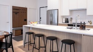 Uma cozinha moderna com uma ilha central, banquetas, geladeira e armários brancos.