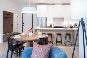 A modern kitchen with white cabinets, a central island, and bar stools. - Bright & stylish 2-bedroom, 2-bath condo in Mackenzie Village—your cozy mountain retreat, just minutes from outdoor adventure, dining, and year-round recreation. (Revelstoke)
