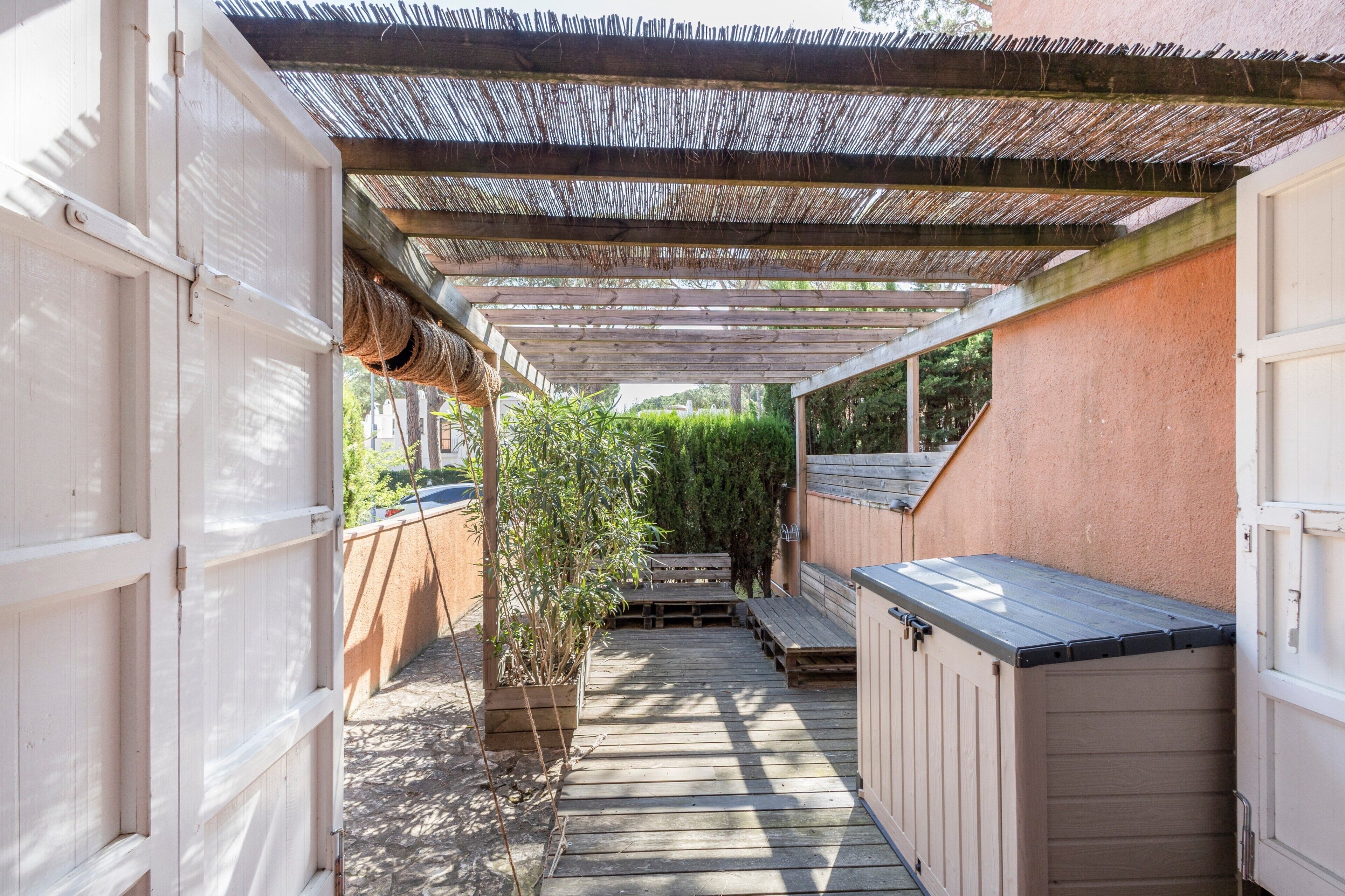 A covered outdoor area with a wooden deck, a bench, a small table, and a storage unit.