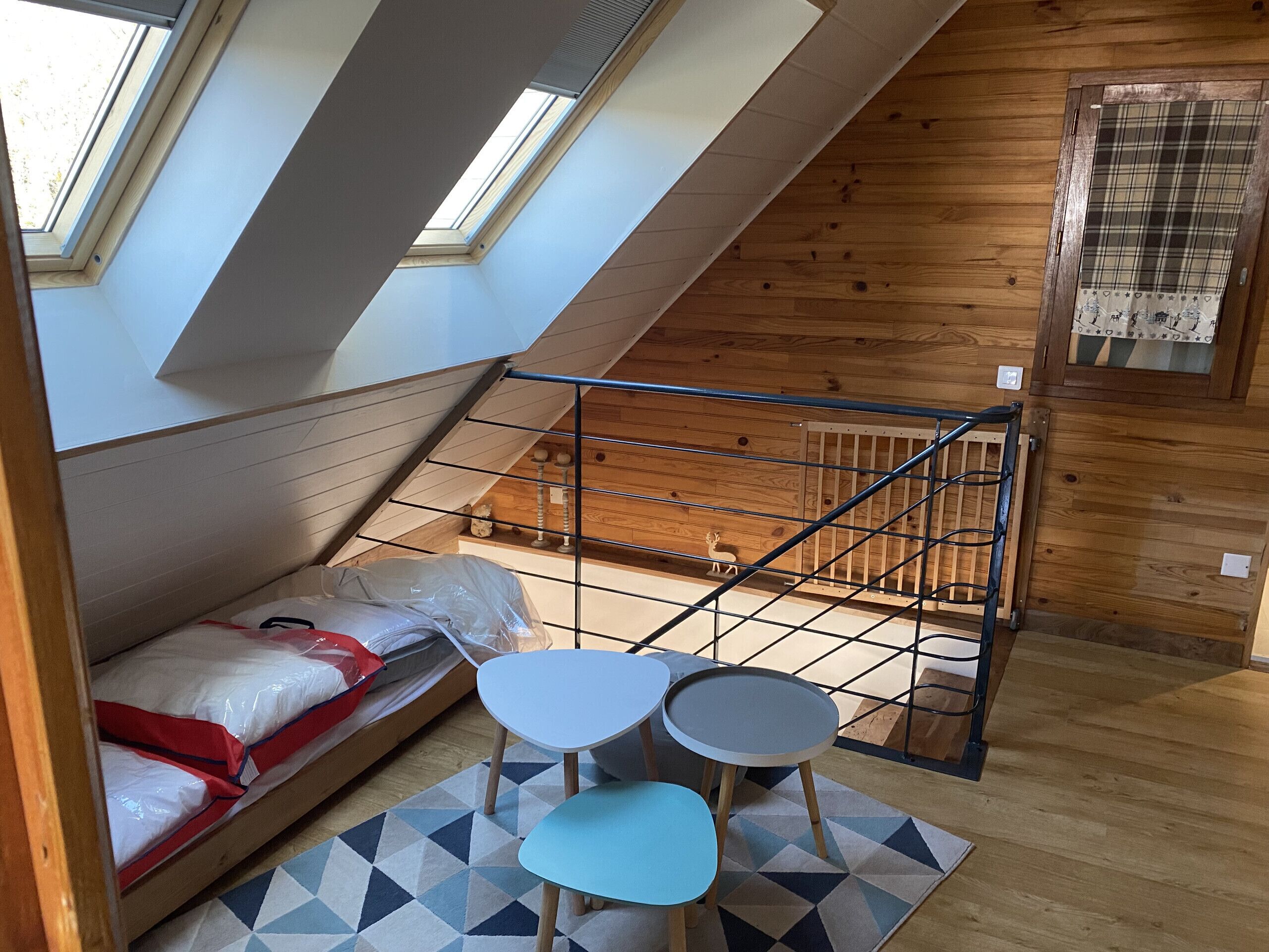 A loft bedroom with a bunk bed, a small table with chairs, a skylight, and a wooden ceiling.