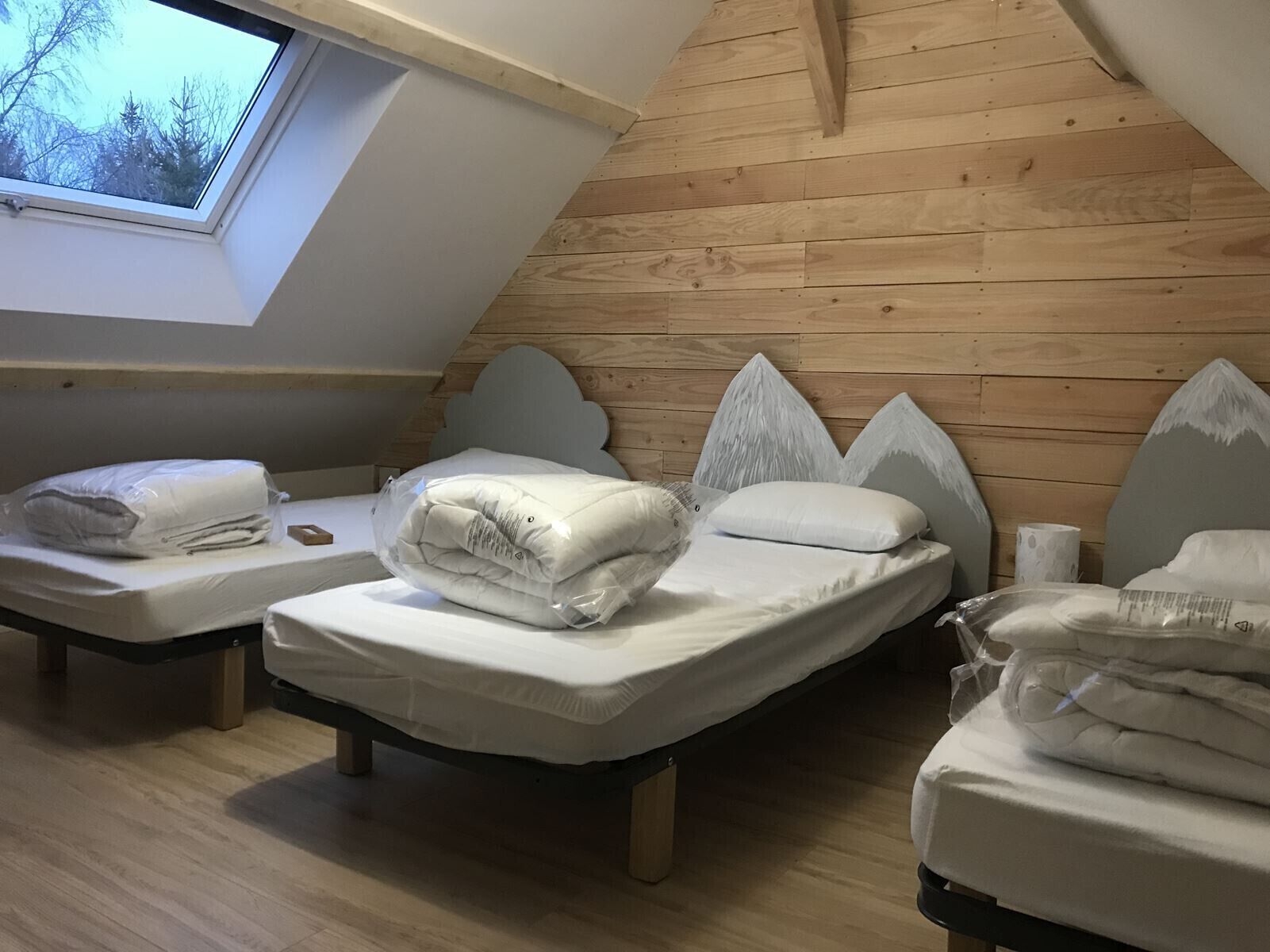 A loft-style bedroom with three beds, wooden slat walls, and a skylight.
