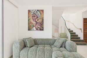 Ein modernes Wohnzimmer mit einem grünen Sofa, einer Holztreppe und einem an der Wand befestigten Kunstwerk.
