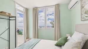 Un dormitorio con cama, ventana, balcón y aire acondicionado.