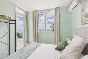 Ein Schlafzimmer mit Bett, Fenster, Balkon und Klimaanlage.