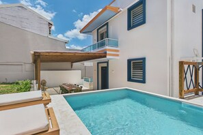 Ein Schwimmbad mit Liegestühlen, einer Holzpergola und einem zweistöckigen Gebäude mit Balkonen.