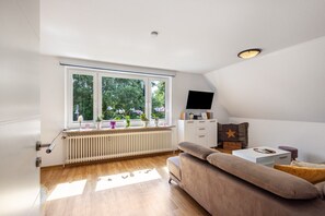 Un salon moderne avec un canapé, un téléviseur et une fenêtre agrémentée de plantes.