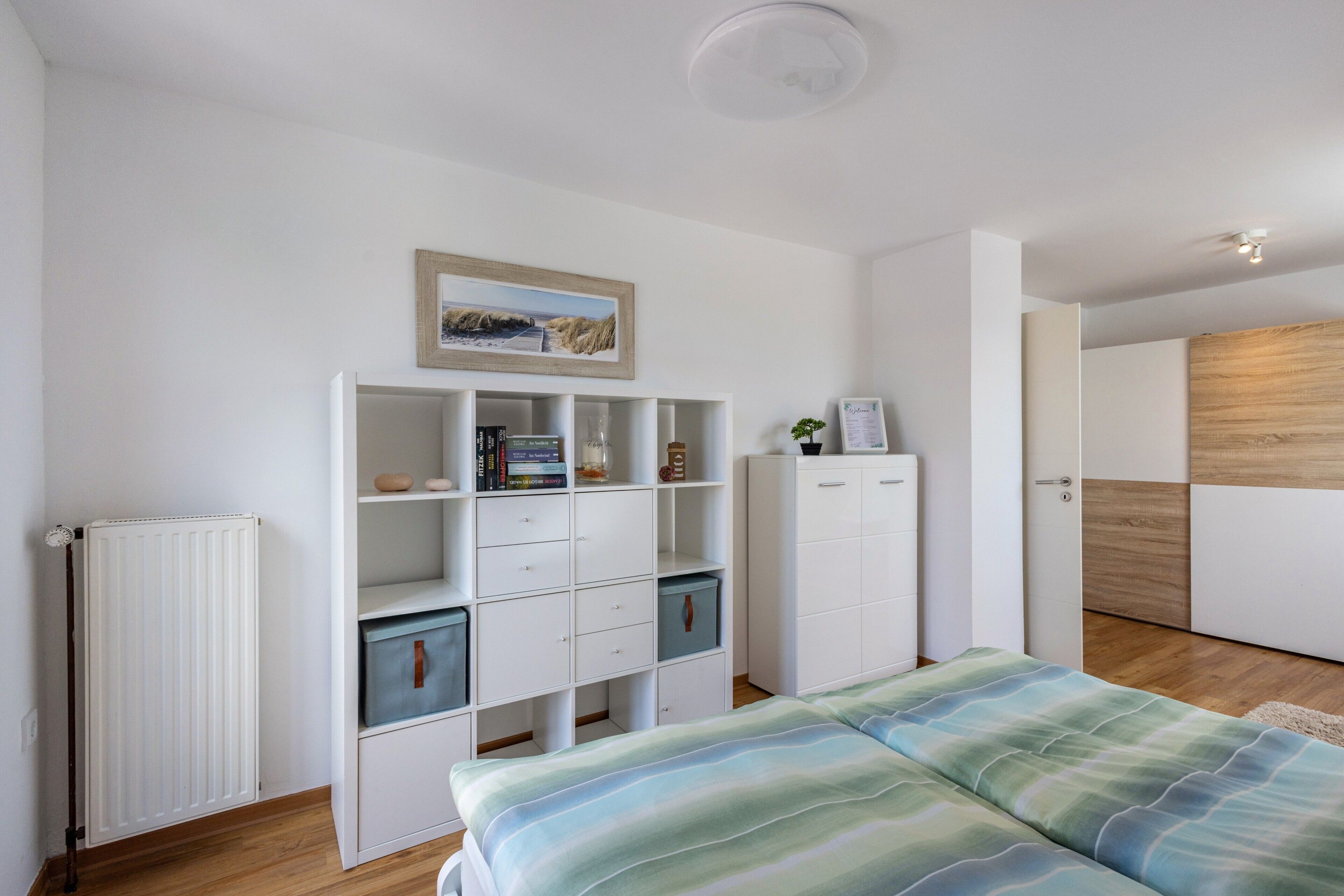 Een slaapkamer met een bed, een witte kast, een radiator en een houten vloer.