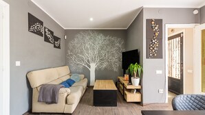 Un salón con sofá, una mesa de centro, televisor y una obra de arte en la pared.