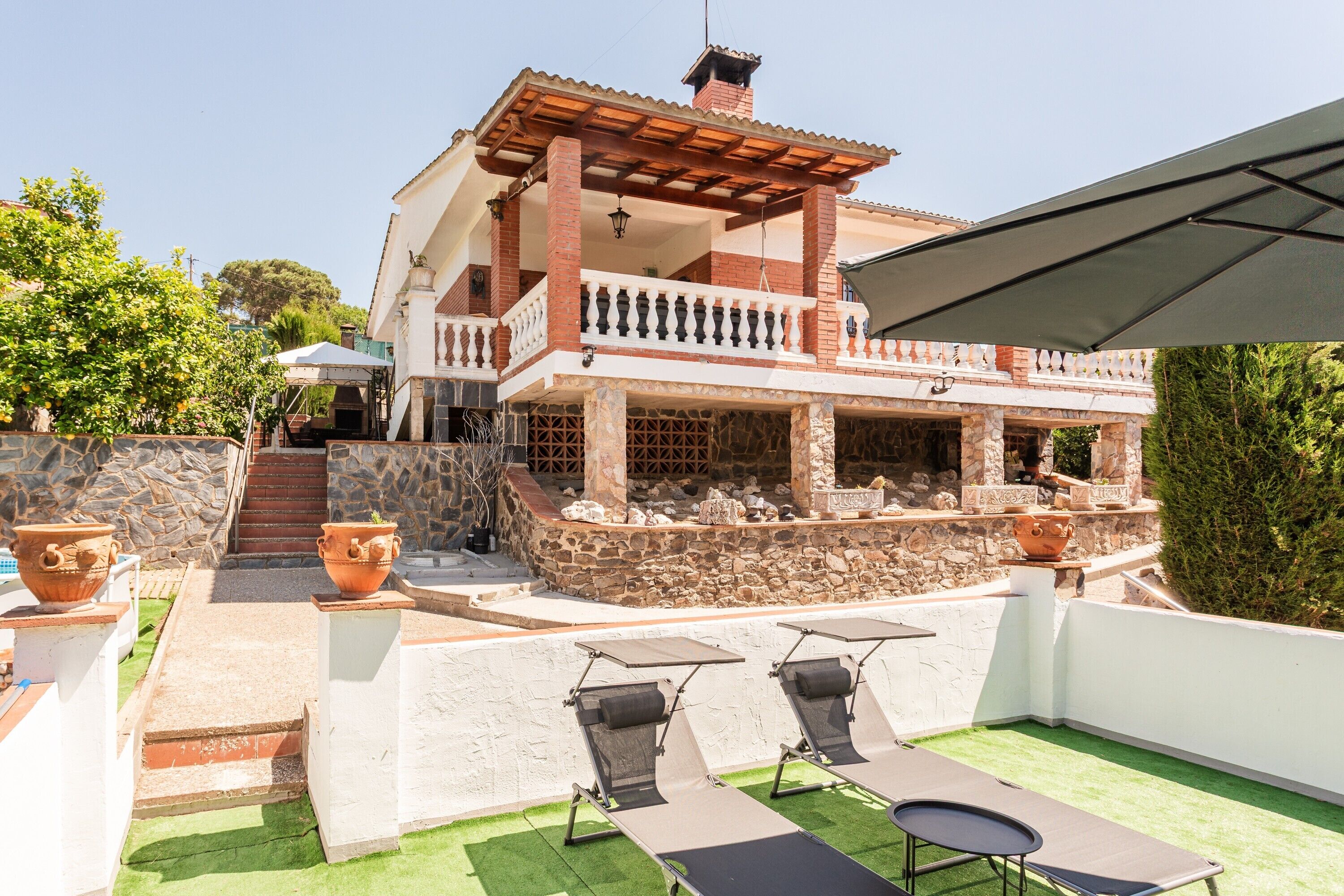 A two-story house with a balcony, outdoor seating, and a stone wall.