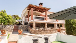 Una casa de dos pisos con balcón, mobiliario exterior y un muro de piedra.