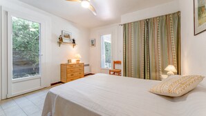 Une chambre à coucher comprenant un lit, une commode, une chaise, un ventilateur de plafond et une fenêtre.