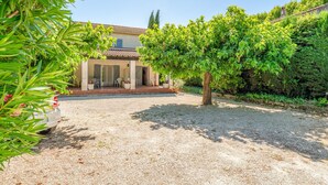 Une maison avec une allée en gravier, un patio couvert et un arbre au premier plan.