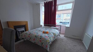 Un dormitorio con cama, una silla, un radiador y una ventana con cortinas.
