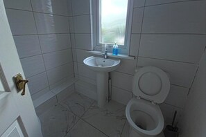 Et badeværelse med hvide fliser, en vask, et toilet og et vindue.