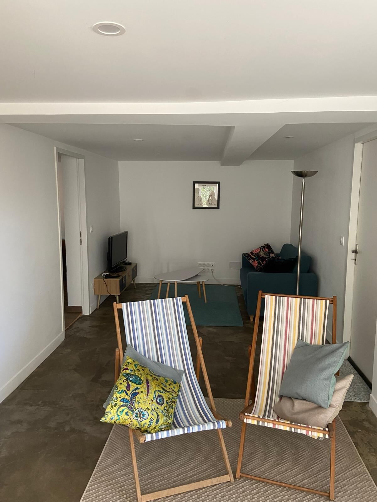 Een woonkamer met twee gestreepte stoelen, een bank, een televisie en een ingelijst schilderij aan de muur.