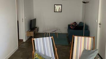 Een woonkamer met twee gestreepte stoelen, een bank, een televisie en een ingelijst schilderij aan de muur.