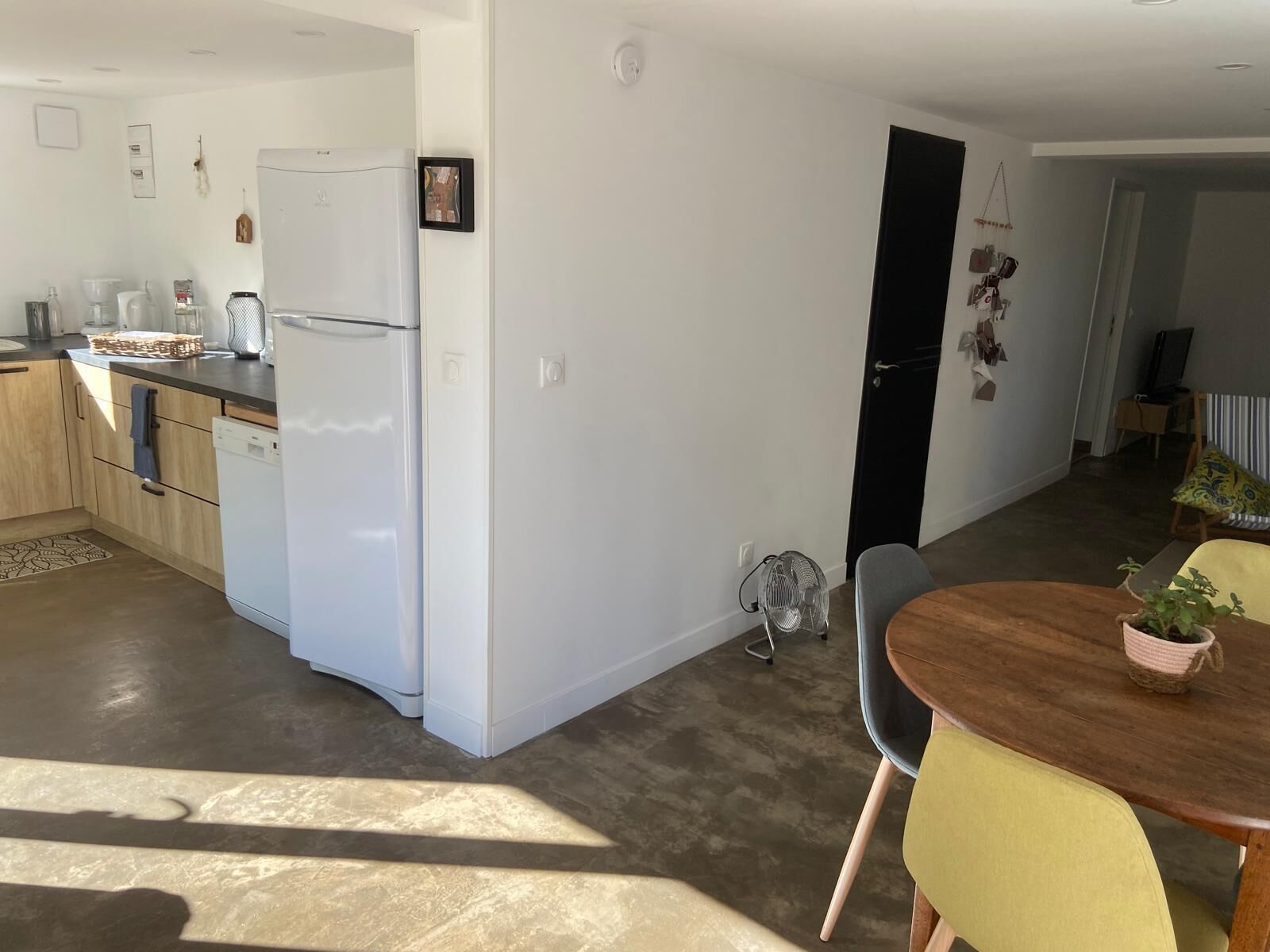 A modern kitchen with white appliances, a dining area with a wooden table and chairs, and a living room with a sofa and a TV.
