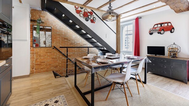 Un comedor con una escalera, una pared de ladrillo y un adhesivo con forma de coche rojo en la pared.