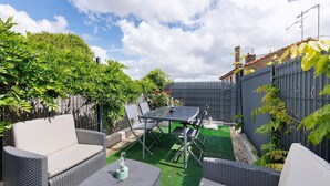 Un patio exterior con una mesa y sillas, rodeado de vegetación y una cerca.