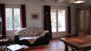 A room with a sofa, a dining table, and a window with curtains. - VAISON LA ROMAINE QUIET LITTLE HOUSE IN THE COUNTRYSIDE (Crestet)