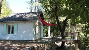 A white building with a stone foundation, a red awning, and a wooden deck. - Small house in the heart of the Cévennes (Concoules)