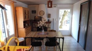 A dining area with a wooden table, chairs, a small yellow table with items, a clock on the wall, and a door leading outside. - Small house in the heart of the Cévennes (Concoules)