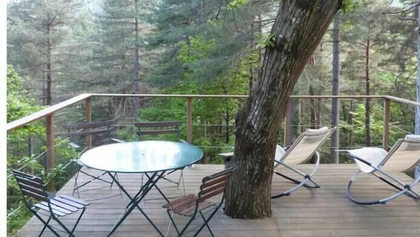 A wooden deck with a table and chairs, surrounded by trees. - Small house in the heart of the Cévennes (Concoules)