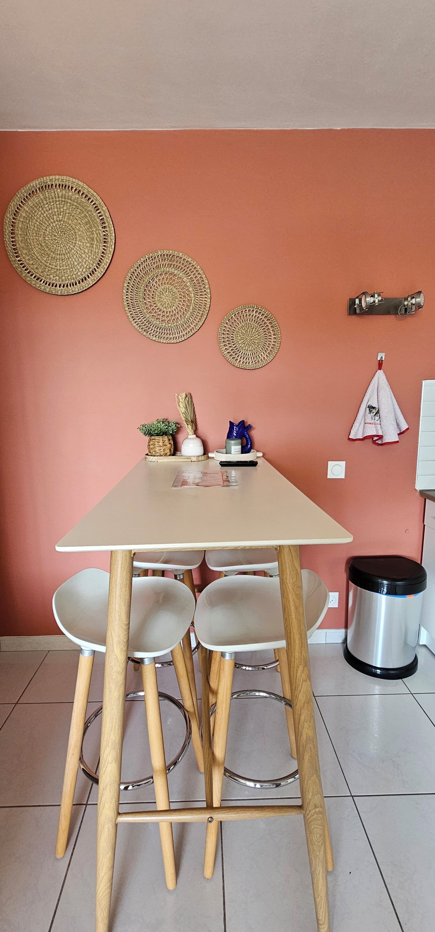 Ein Essbereich mit einem Tisch, vier Stühlen, einem Mülleimer und Wanddekorationen.