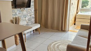 Een woonkamer met een stenen muur, een flatscreen televisie, een bank, een eettafel en een kroonluchter.
