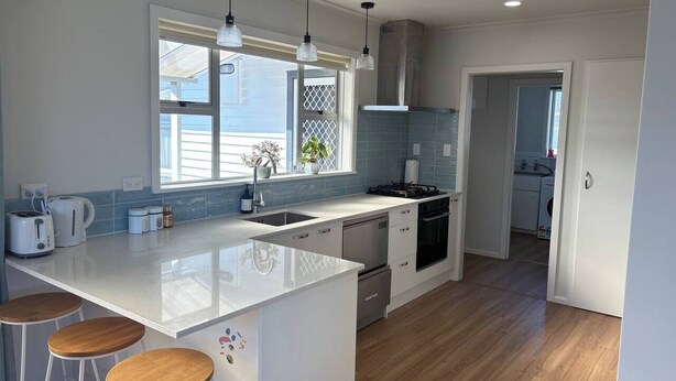 A modern kitchen with a central island, bar stools, a stove, and a sink.