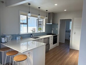 A modern kitchen with a central island, bar stools, a stove, and a sink. - Hawke’s Bay Basecamp (Napier)
