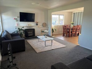 Een woonkamer met een bank, salontafel, open haard, televisie en een eethoek met stoelen.
