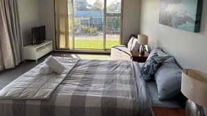 A hotel room with a bed, a TV, a desk, a lamp, and a painting.