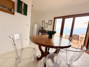 A dining area with a wooden table and clear chairs, a green bowl on the table, and a view of mountains through a glass door. - Frida's Home by Theater Home - with big terrace and marvellous lake view (Tignale)