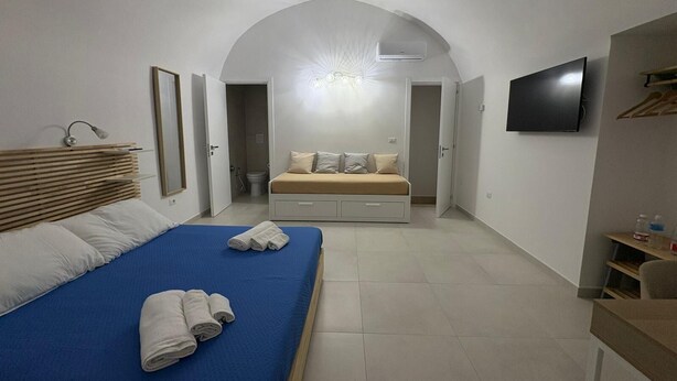 Un dormitorio moderno con una cama grande, una cama más pequeña, un televisor y una zona de ducha.