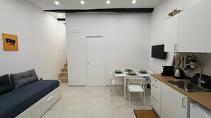 Un espacio habitable compacto con sofá, mesa de comedor, sillas, área de cocina con fregadero y televisor.