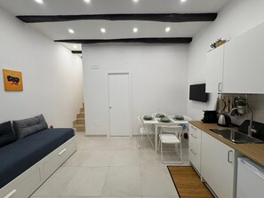 Ein kompakter Wohnbereich mit Sofa, Esstisch, Stühlen, Küchenzeile mit Spüle und Fernseher.