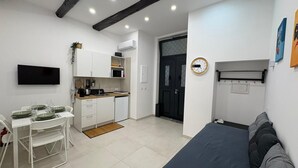 Un espacio habitable compacto con kitchenette, un área de comedor con mesa dispuesta para cuatro, un sofá y un reloj montado en la pared.