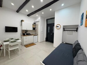 Ein gemütlicher Wohnbereich mit Küchenzeile, einem Essbereich mit Tisch für vier Personen, einer Couch und einer an der Wand befestigten Uhr.