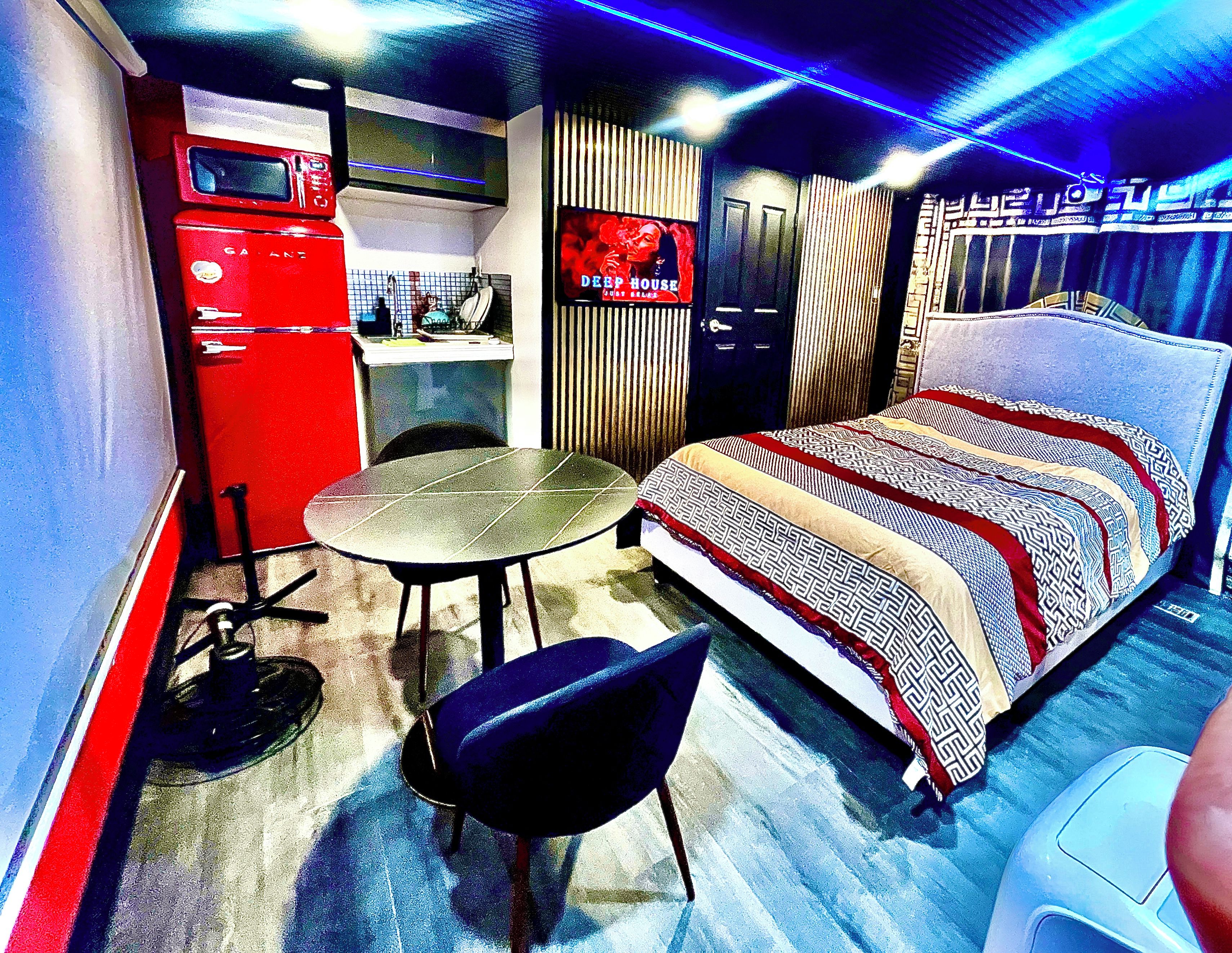 Ein kleines Hotelzimmer mit Bett, einem Tisch, einem Stuhl, einer Küchenzeile und einem Kleiderschrank.