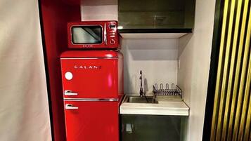 A compact kitchenette with a red refrigerator, a microwave, and a sink.