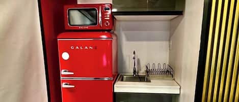 Una kitchenette compacta con un refrigerador rojo, un microondas y un lavamanos.