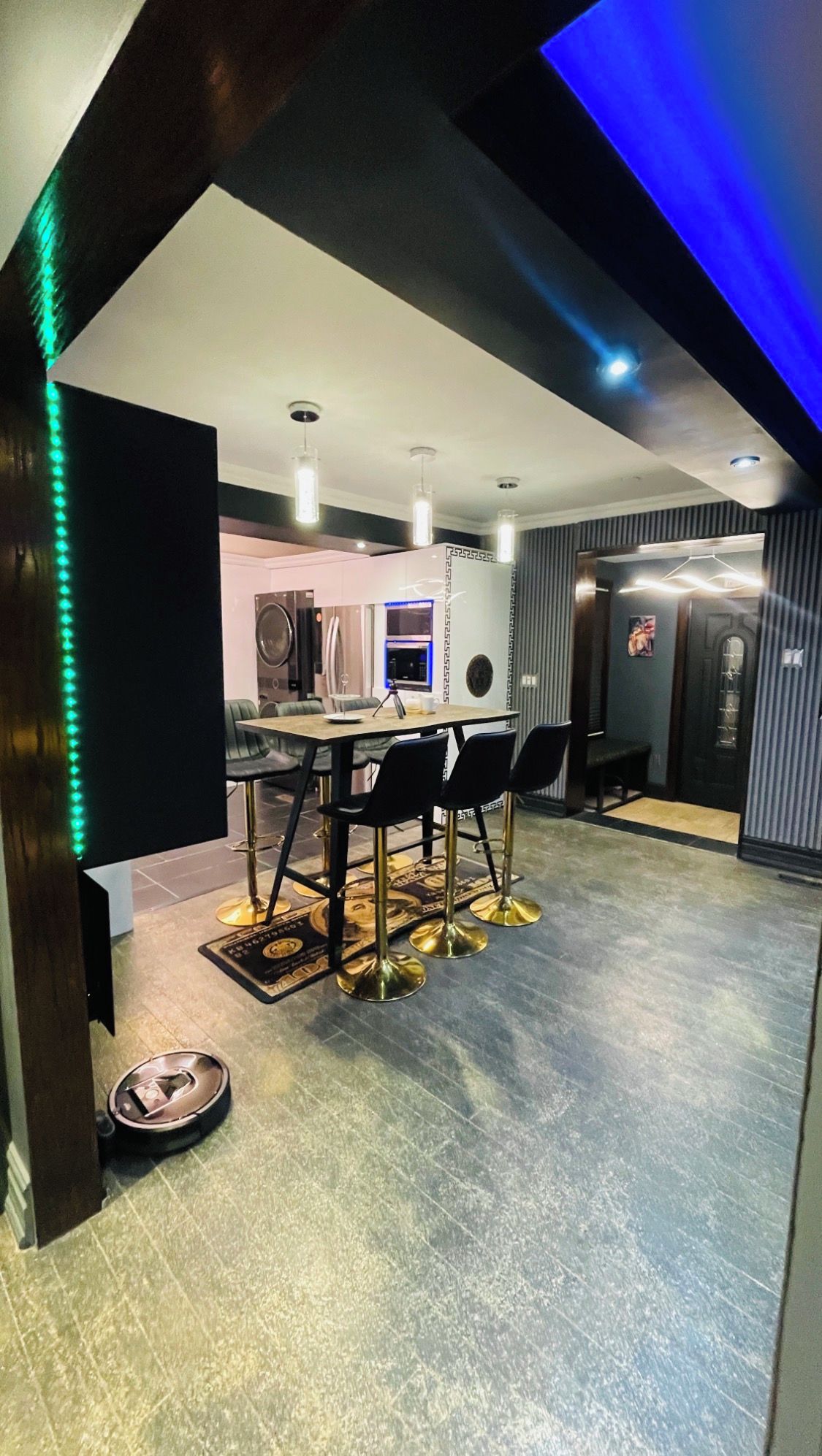 A modern kitchen with a dining area, featuring a central island, pendant lighting, and a patterned rug.