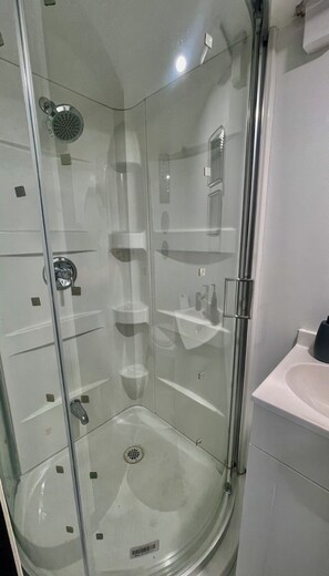 Box de chuveiro com vidro, chuveiro manual, porta de vidro e pia branca com espelho.