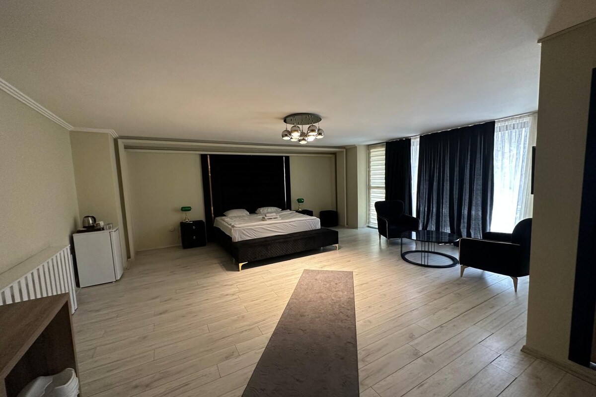 A modern hotel room with a large bed, a desk, a chair, and a view of the city.